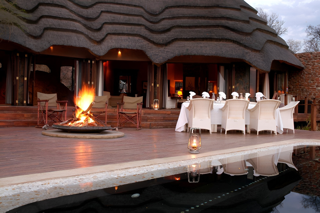 All-weather outdoor dining furniture set supplied by Bellagio Interiors at a Madikwe game lodge beside a safari fire at sunset
