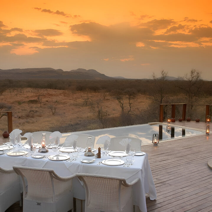 All-weather outdoor dining furniture set supplied by Bellagio Interiors at a Madikwe game lodge beside a safari fire at sunset